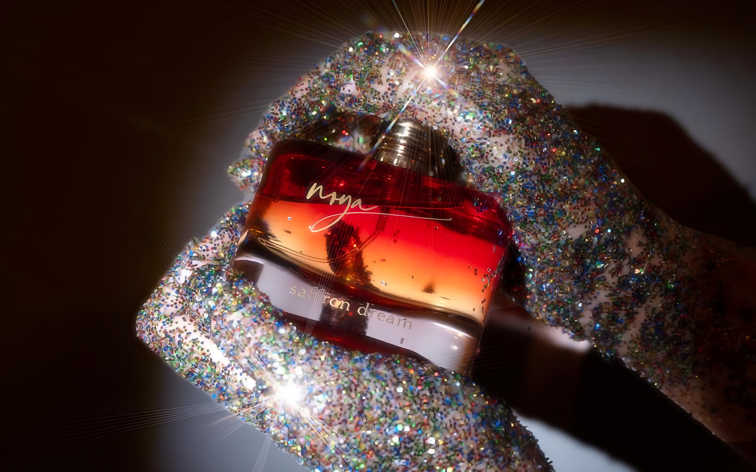 Noya Saffron Dream perfume bottle held by hands adorned with glitter.