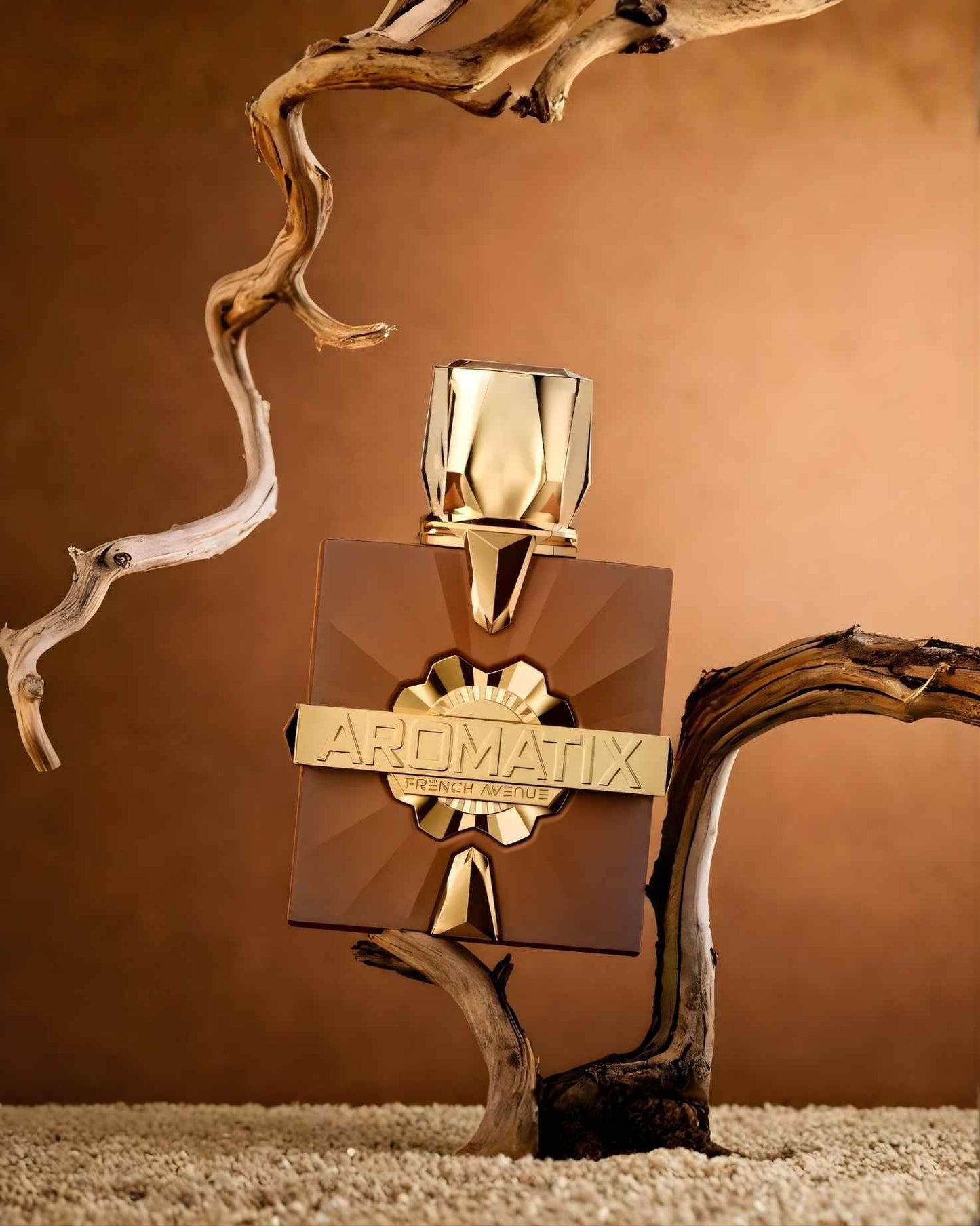 Aromatix Royal Taboo ExDP by French Avenue perfume bottle artistically staged between weathered wooden branches on a textured sandy base with a warm brown background.
