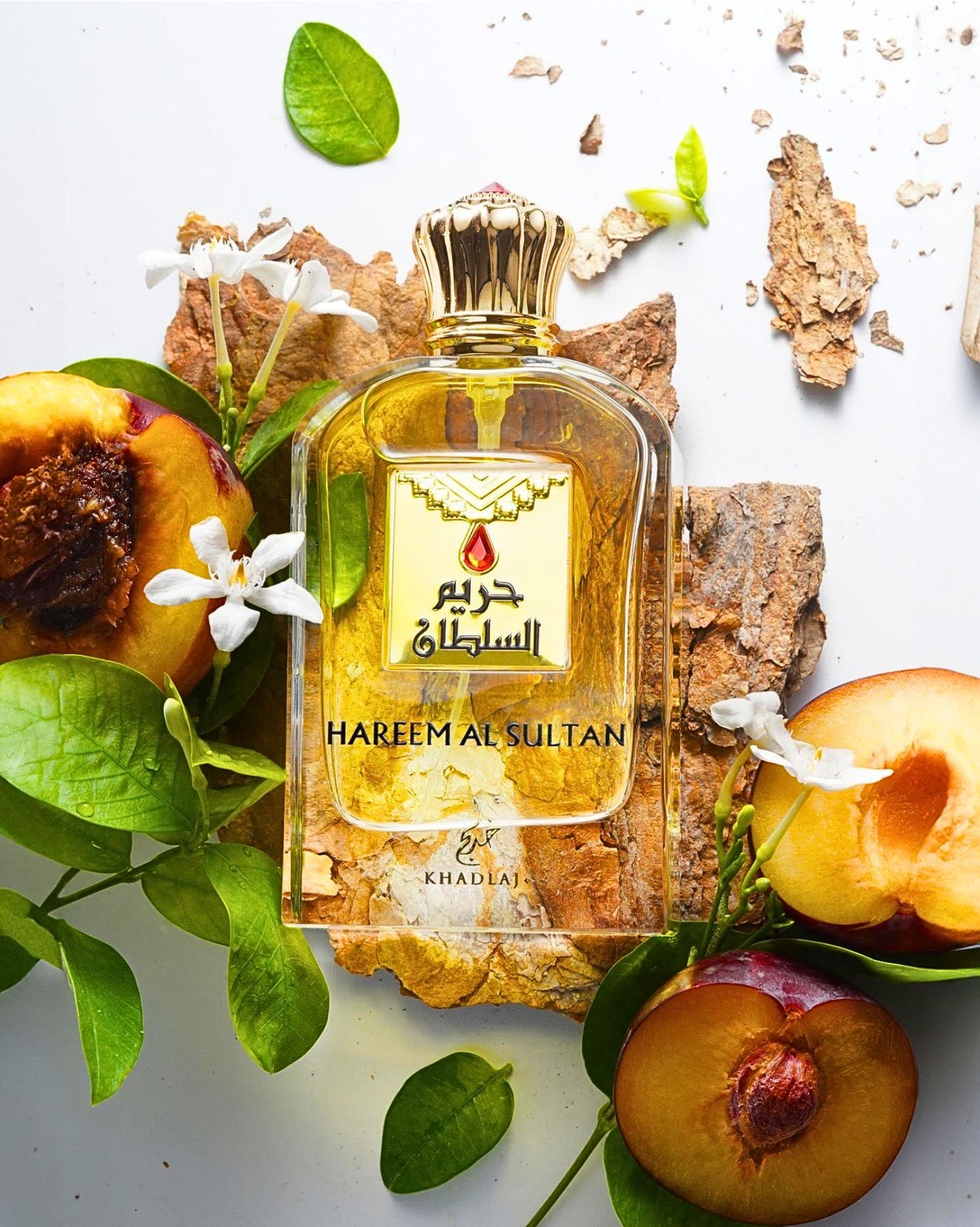 hareem-al-sultan-gold-eau-de-perfume-bottle-laying-over-wood-surrounded-by-peach-and-leaf