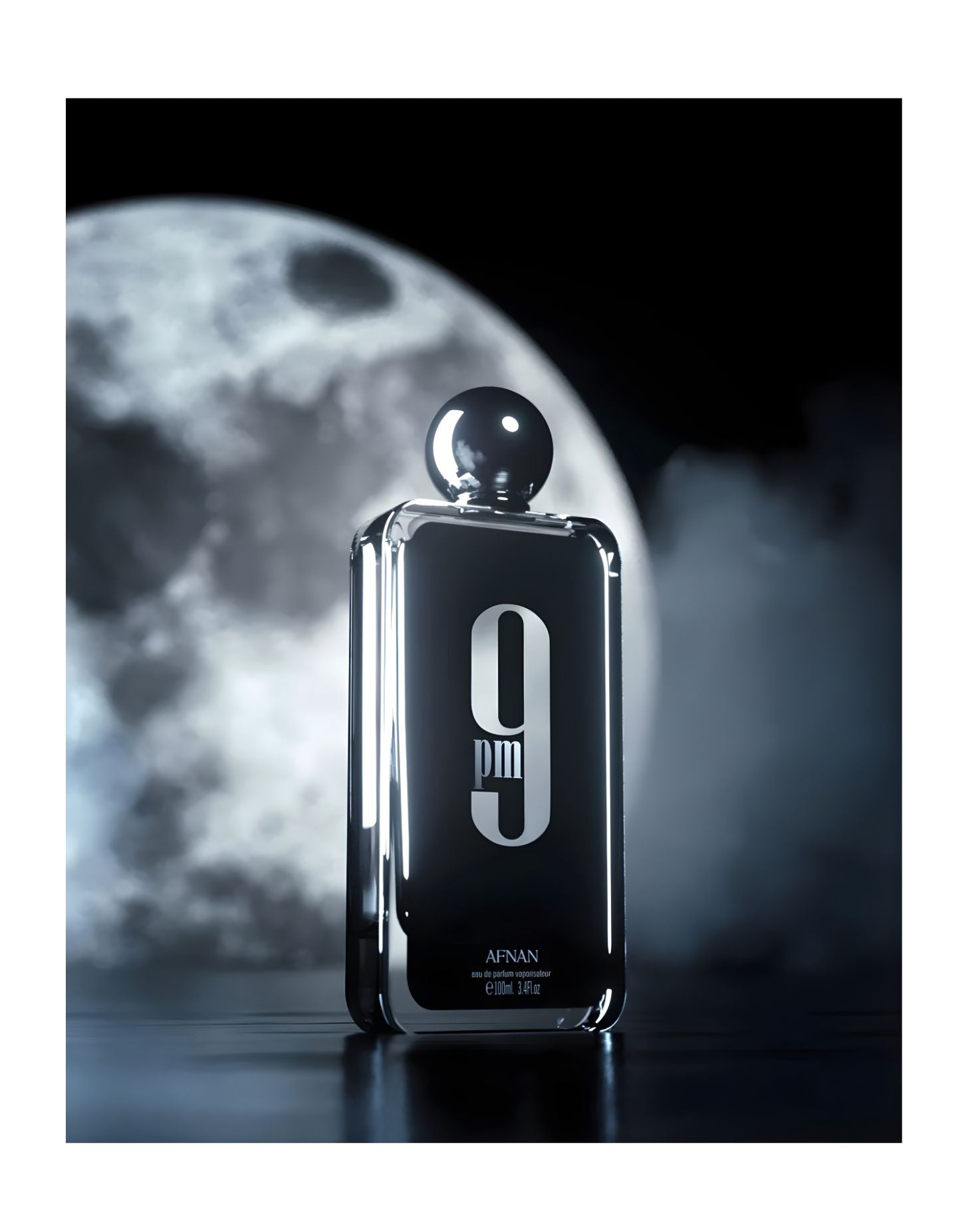 A dramatic, low-light photograph of a rectangular glass bottle of Afnan 9 PM Eau de Parfum, 100ml / 3.4 fl.oz., standing on a dark, reflective surface. The background features a large, luminous, detailed full moon partially obscured by mist or clouds, emphasizing the fragrance's evening theme.