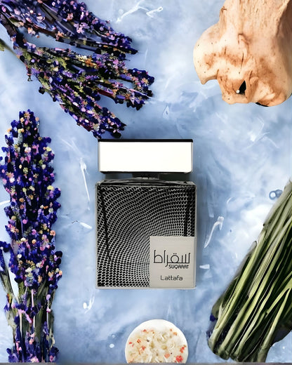 An artistic still life featuring the Lattafa Jasoor bottle surrounded by a red apple, sliced lime, and lavender on a painterly background.