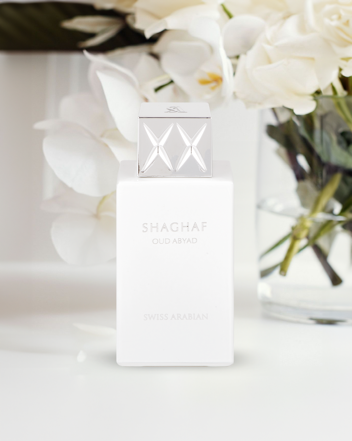 Swiss Arabian Shaghaf Oud Abyad perfume bottle in elegant white with silver cap displayed among soft white orchid flowers