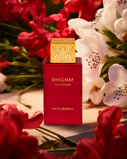 Vibrant red bottle of Swiss Arabian Shaghaf Oud Ahmar perfume with golden cap set against a backdrop of lush red tulips and delicate white flowers.