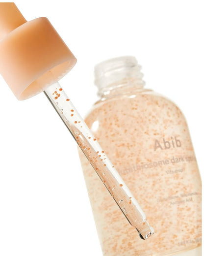 Close-up of a glass dropper pulling out the Abib Vita Drop serum, showing the suspended, small, light-orange capsules inside the bottle.