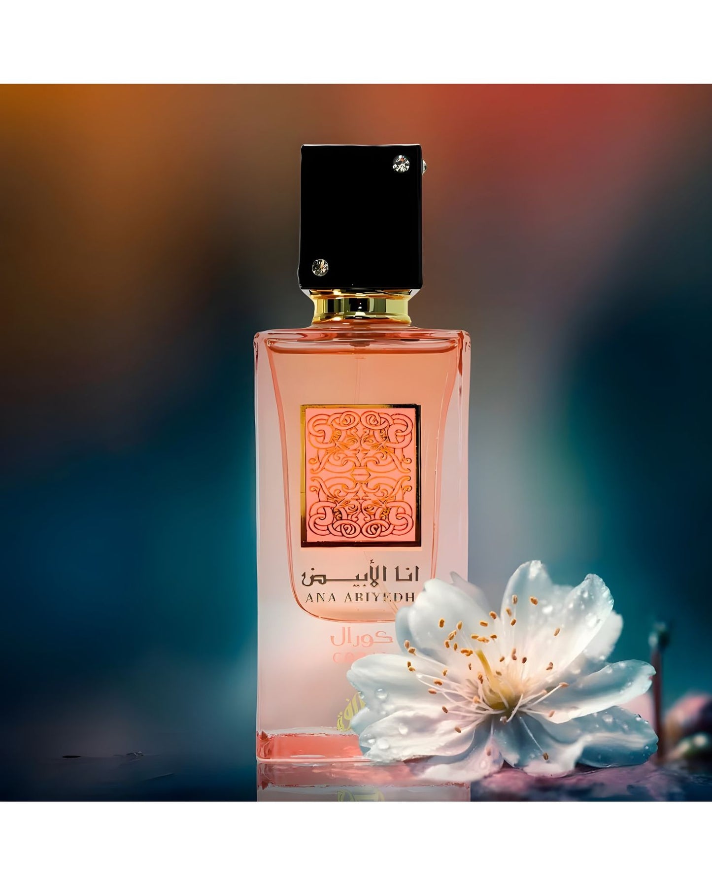 The Ana Abiyedh Coral perfume bottle, with its pink liquid and ornate label, is featured prominently with a single white flower with water droplets in the foreground. The background is a dramatic, blurred mix of dark teal, blue, and amber tones.