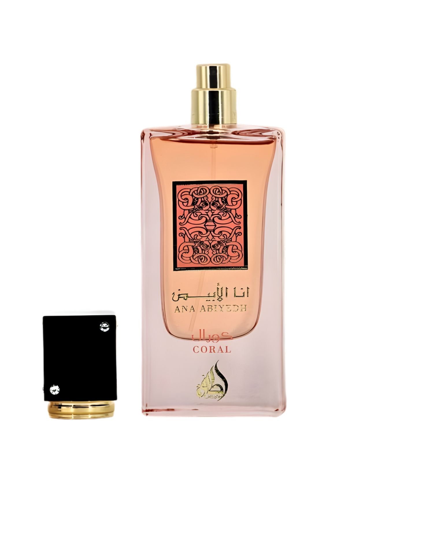 A rectangular perfume bottle with pink liquid that gradients to clear glass at the base. The front label is coral pink with ornate dark brown Arabic calligraphy and the text 'ANA ABIYYEDH CORAL'. The black and gold cap sits detached beside the bottle on a light, marble-like surface.