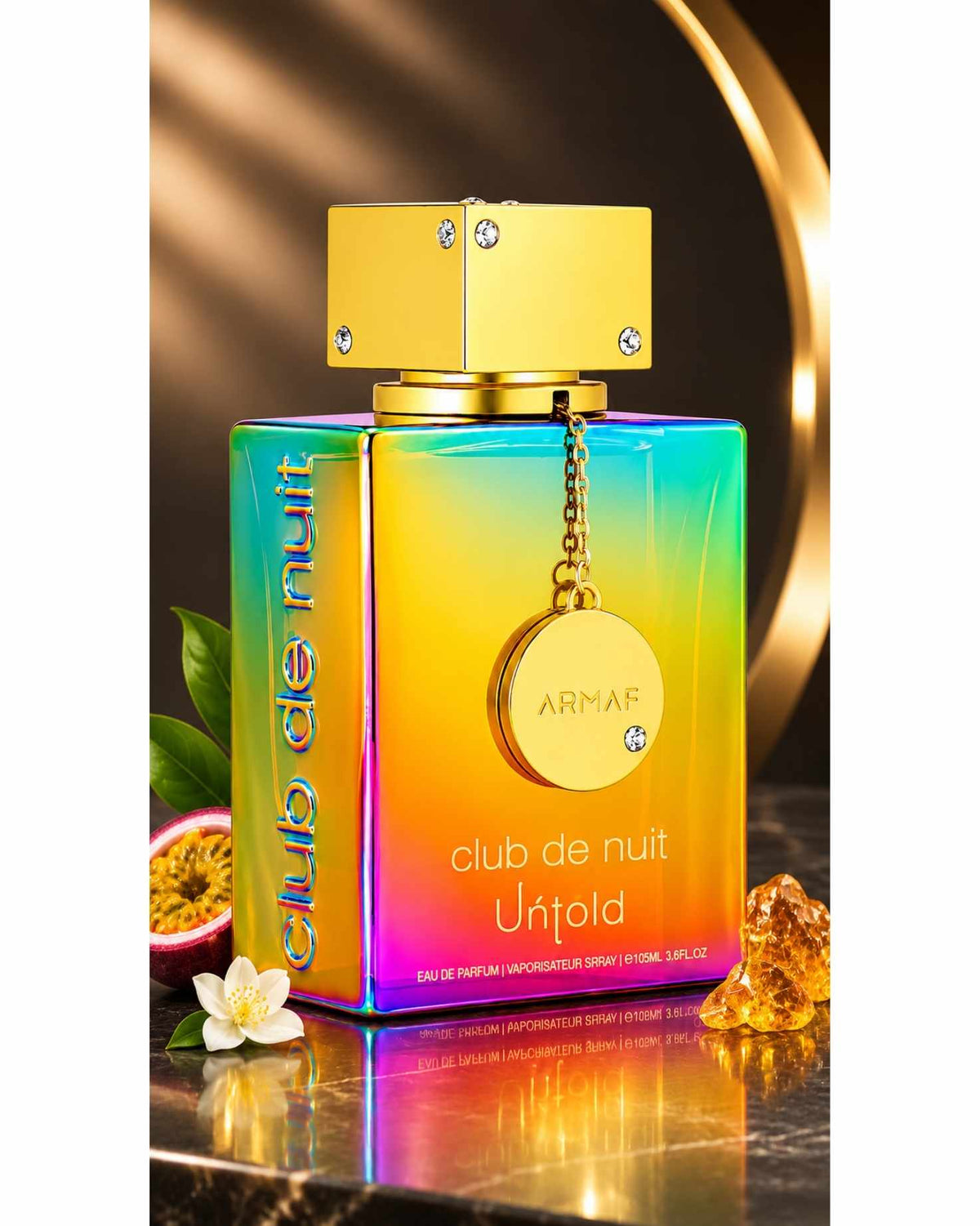 Close-up shot of the Armaf Club de Nuit Untold Eau de Parfum bottle displaying its rainbow gradient finish, gold cap, hanging medallion, sliced passion fruit, white jasmine blossom, and amber crystals.