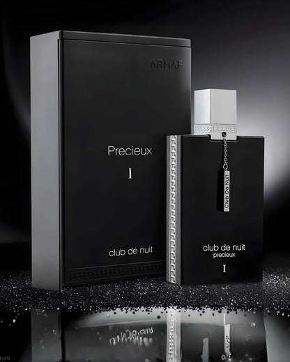 A high-contrast, black and silver still life product shot of the Armaf Club De Nuit Precieux 1 EXdp perfume bottle and its luxury rectangular box on a reflective surface with sparkling glitter.