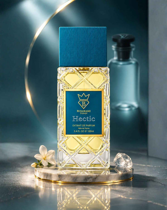 Bujairami Hectic Extrait de Parfum bottle on a circular marble podium with a white blossom flower and a clear faceted crystal on a reflective surface.