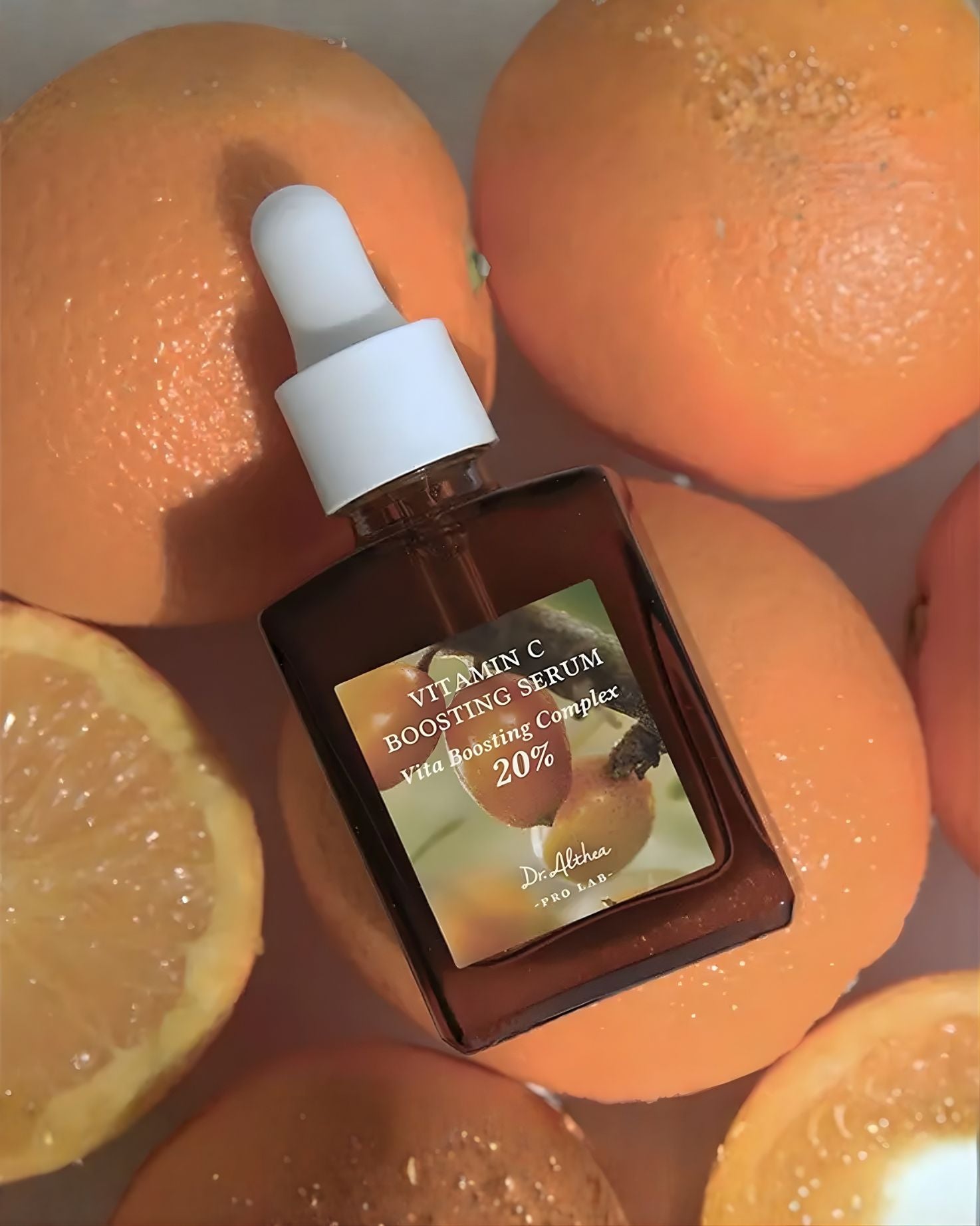 Close-up of a Dr. Althea Vitamin C Boosting Serum bottle lying among several whole and sliced oranges.