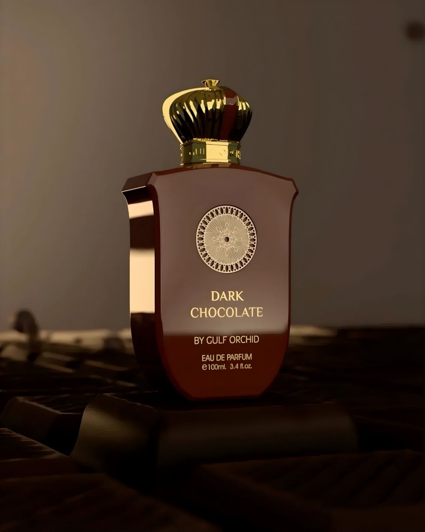 A bottle of Dark Chocolate by Gulf Orchid perfume resting on pieces of real dark chocolate, highlighting the gourmand scent notes and gold crown cap.