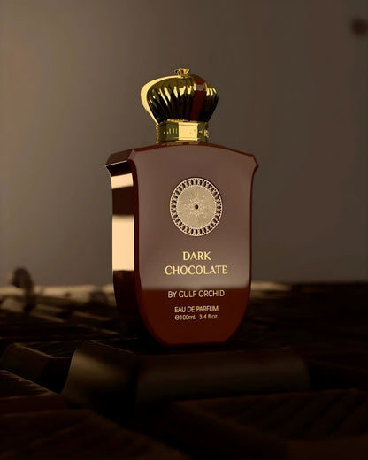 A bottle of Dark Chocolate by Gulf Orchid perfume resting on pieces of real dark chocolate, highlighting the gourmand scent notes and gold crown cap.