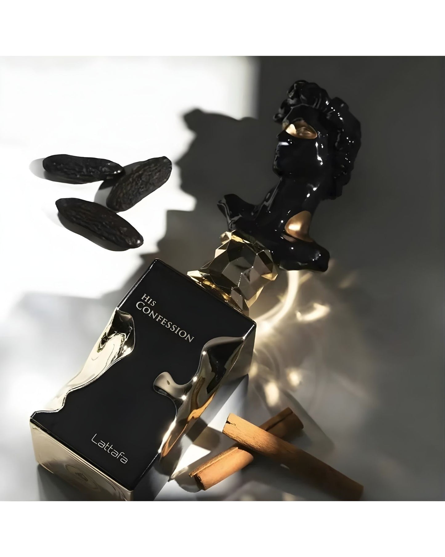 Close-up of Lattafa His Confession perfume bottle, featuring a black and metallic gold design, next to a black sculpture of a classical bust, whole tonka beans, and cinnamon sticks, highlighting the rich, spicy notes.