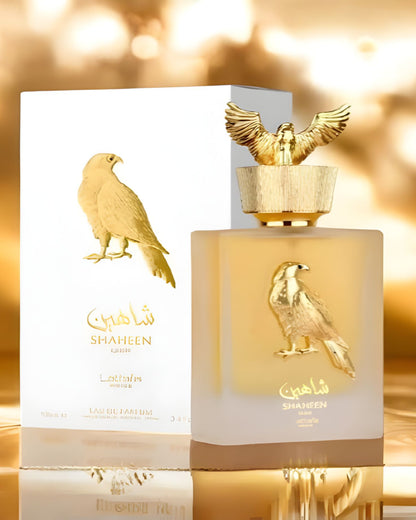 Front view of the Lattafa Shaheen Gold edp perfume bottle and its elegant white and gold retail box, set against a shimmering gold bokeh background.