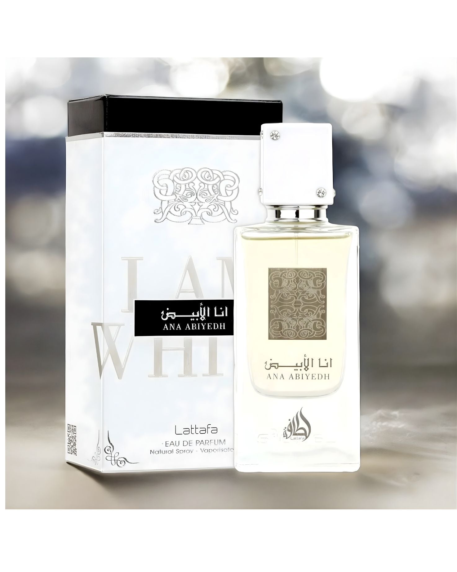 The Lattafa 'Ana Abiyedh' Eau de Parfum bottle, clear with colorless liquid and a white cap, is displayed next to its matching white box. The box features large embossed details and the name in both Arabic and English ('ANA ABIYYEDH' and 'I AM WHITE'). The background is a blurred, sparkling bokeh effect.