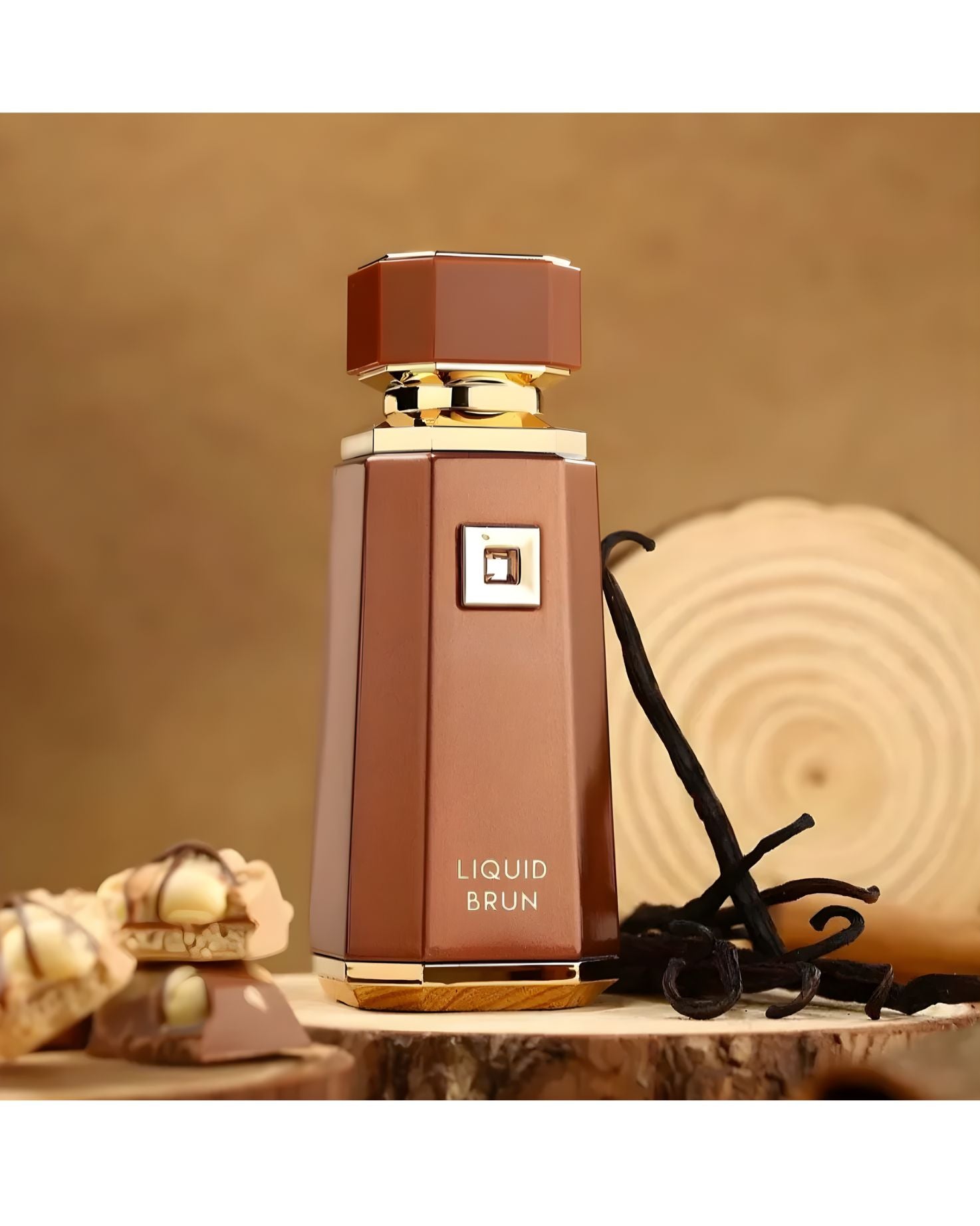 The Liquid Brun Eau de Parfum bottle, brown and gold, stands on a rustic wooden surface next to several dark vanilla bean pods and a stack of chocolate and hazelnut sweets. A light brown, wood-grain background is visible.