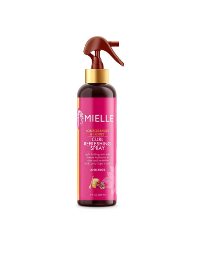 A bottle of Mielle Pomegranate & Honey Curl Refreshing Spray. The dark brown bottle has a gold neck and a brown trigger sprayer. The pink label states "POMEGRANATE & HONEY CURL REFRESHING SPRAY" and describes it as a "light holding mist with intense hydration to reactivate and redefine thick, curly Type 4 curls" and is "ANTI-FRIZZ.