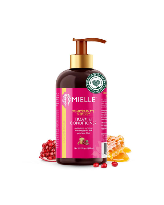 A black pump bottle of Mielle Pomegranate & Honey Leave-In Conditioner with a bright pink label. The label highlights the product's function to 'Maintain curl pattern and detangle for thick, curly Type 4 hair.' The bottle is framed by fresh pomegranate seeds and a piece of dripping honeycomb, isolated on a white background.