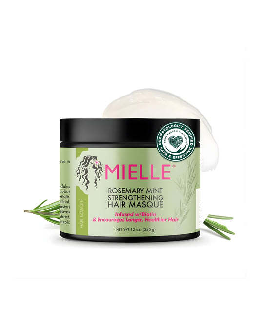 The Mielle Rosemary Mint Strengthening Hair Masque jar, featuring a black lid and a green label with rosemary illustrations. A dollop of white masque product is visible on top, and sprigs of fresh rosemary frame the jar. The label indicates it is 'Infused w/ Biotin & Encourages Longer, Healthier Hair' and is 'DERMATOLOGIST VERIFIED,' isolated against a white background.