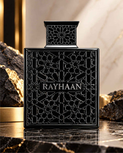 Rayhaan Obsidian Eau de Parfum black geometric latticed bottle displayed on polished dark marble beside black volcanic stones with gold accents.