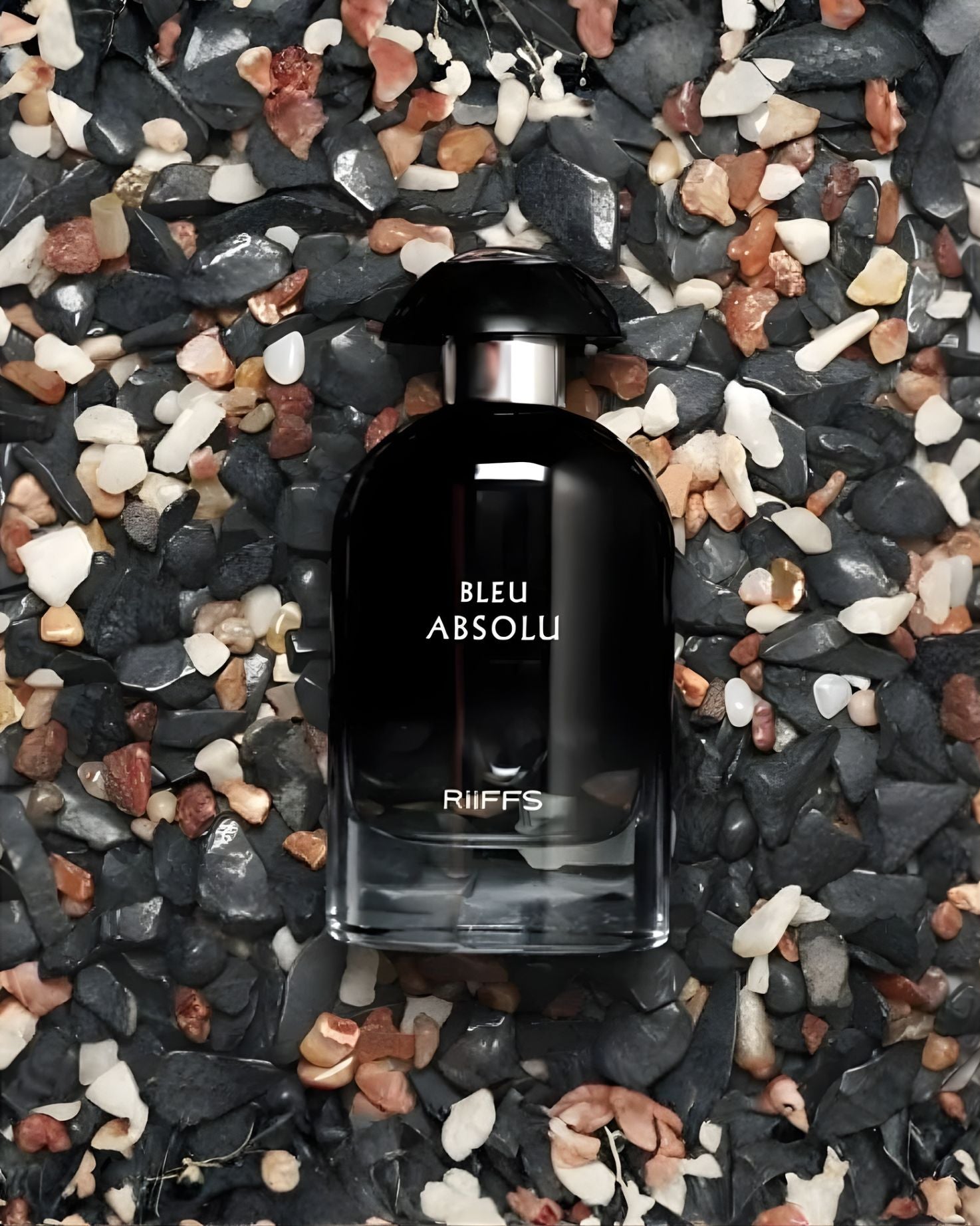 lose-up of the RiiFFS Bleu Absolu edp fragrance bottle sitting on a bed of dark, white, and reddish-brown decorative pebbles.