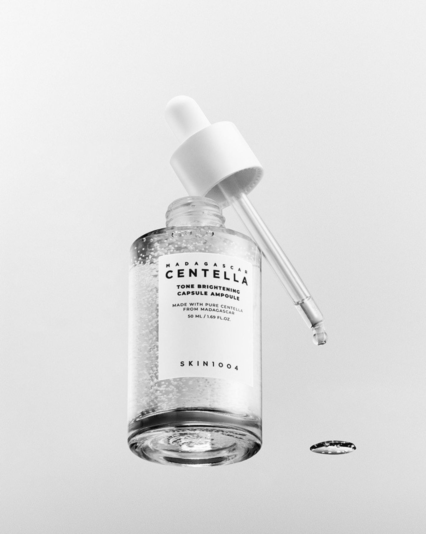 Small clear glass dropper bottle (30 mL) of SKIN 1004 Madagascar Centella Tone Brightening Capsule Ampoule with a white cap, showcasing the visible white capsule particles within the serum.